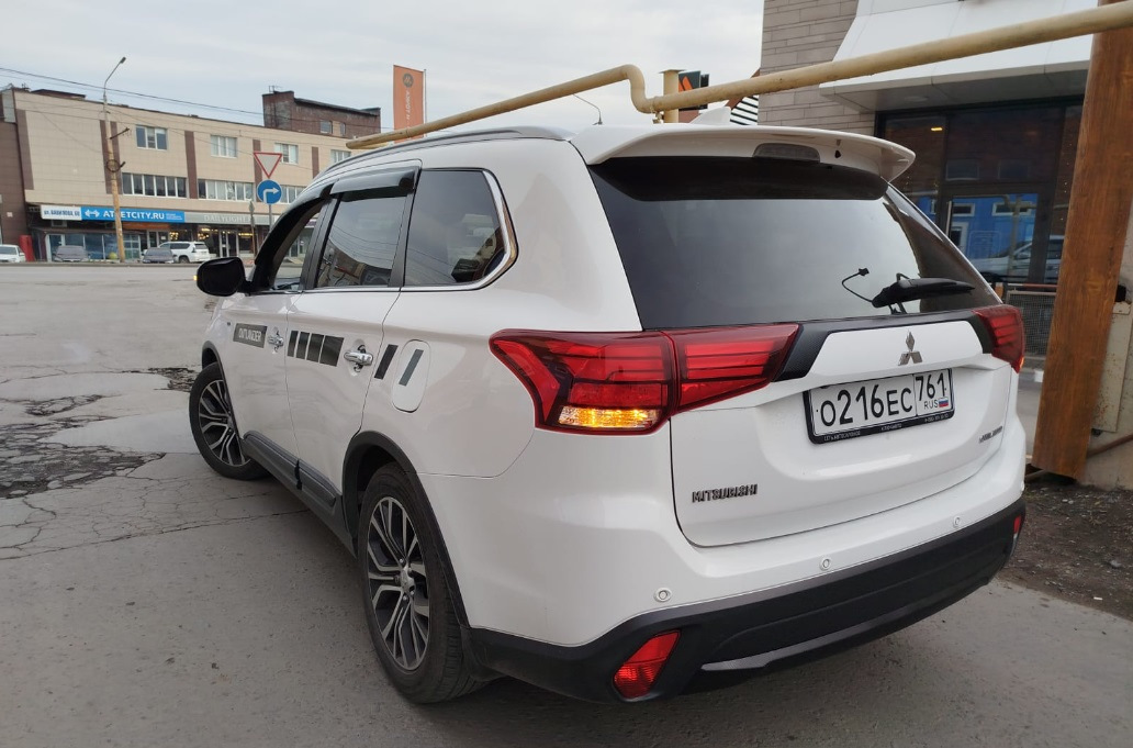 Спойлер — один из немногих элементов стайлинга для Outlander, который вызывает минимум споров — разумеется, с ним лучше, чем без него :)


Со спойлером теперь
Итак, заказал на Али сразу крашеный… По прикидкам некрашеный+покраска (зато точно в цвет) получалась примерно в 15Круб. Окрашеный сразу в белый — 4,3Круб. Решил рискнуть.

Пришел спойлер в транспортную компанию упакованный в пузырчатую пленку основательно, как мумия :)
И, тем не менее — сурпрыз! Заметный залом на внешнем ребре :(


Ну как так?
Ну в той 10-сантиметровой толщины обертке вряд ли так могло получиться, скорее всего сразу таким положили.
В-общем, подал спор (изначально подумал, что оспоренный деньги отдам мастерам, чтобы шпатлевали и красили). Отспорил 1,8Круб. То есть спойлер с дефектом обошелся в 2,5Круб.


По цвету — очень хорошее попадание, разве что на спойлере есть примесь блестящая (наверное, это Polar White или как его там). Но с завода бампера от кузова отличаются существенно сильнее :)
Уже начал у знакомых спрашивать, кто занимается такими работами, никто не признавался… повертел-покрутил в руках и решил кое-что попробовать :)

Сделал технологическое отверстие на внутренней стороне, обмотал изолентой наконечник длинной отвертки, нагрел спойлер в теплой воде, арендовал у жены фен и поставил его на минимальный нагрев.
Ну и изнутри минут за 30 осторожненько выровнял дефект.


Технологическое отверстие и инструмент
Пару недель спойлер отлежался на балконе (проверил, не сработает ли эффект памяти у пластика, когда остынет). Дефект проявился прям минимально (и то, это я знал, куда смотреть). Еще минут 10 повторил процедуру поддавливания и нагрева — и вуаля! Результат отличный.


Живьем вообще место дефекта не найдешь
Следующим квестом оказалось прикрепление.
Дальнейший текст скорее всего будет более интересен ростовчанам…

Беглый поиск стекольного герметика и праймера показал, что это добро обойдется в пару тысяч, не меньше. И потом почти весь герметик все равно на выброс…
Заехал в пару мест, где устанавливают стекла. В одном (федеральная сетка, АвтоТрейд) сразу сказали, что у них нет такой услуги в прайсе, а "внепрайсовые работы" караются штрафом и вплоть до увольнения. Но общались вежливо.

В другом (с довольно живыми социальными сетями, вроде как позиционирующие себя положительно, Автостекла на Вавилова) — просто вышел чувак, ни здрасте, ни досвидания, просто сказал "нет, я это делать не буду" и развернулся. Резкий контраст с социальными сетями. Неприятный осадочек :)

Уже подумал — ну всё, придется самому материалы покупать и звать кого-нибудь на помощь для ровной установки. Но решил заглянуть к еще одним установщикам автостекол. Оказалось, неподалеку есть AG Experts. Ребята красавчики — и пообщались вежливо, и один парень вышел посмотрел-пощупал спойлер. Согласились сделать. Подошли прям очень профессионально — все обезжирили, нанесли праймер, погрели феном и спойлер и крышку багажника, нанесли герметик, приклеили спойлер. И стоимость услуги нормальная — 1,5Круб.


Кепка
В-общем, теперь Белый Бумбр со спойлером.
Считаю, что он делает внешний вид аута существенно гармоничнее. Плюс стоимость доработки получилась ну очень приятной.